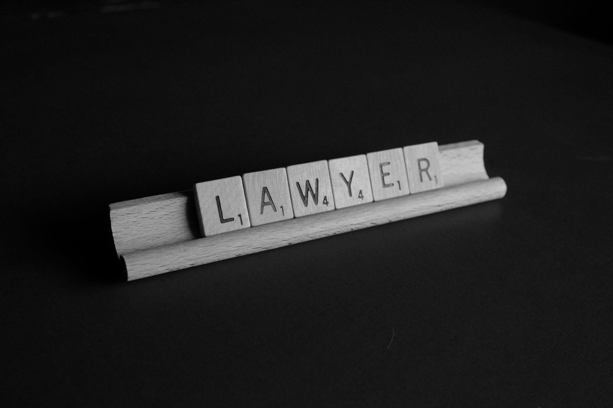 Wooden letter tiles spelling LAWYER on a tile rack against a black background, in black and white